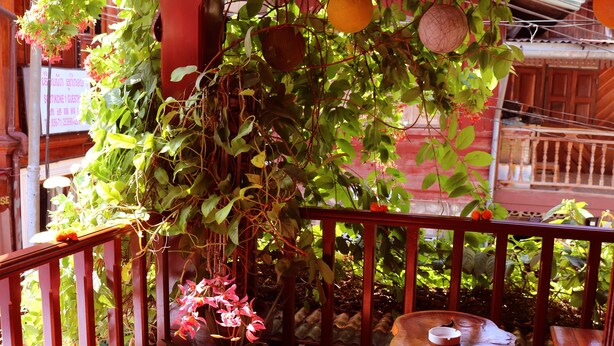 A wooden balcony with potted plants and a small table. - Apple Guesthouse (Luang Prabang)