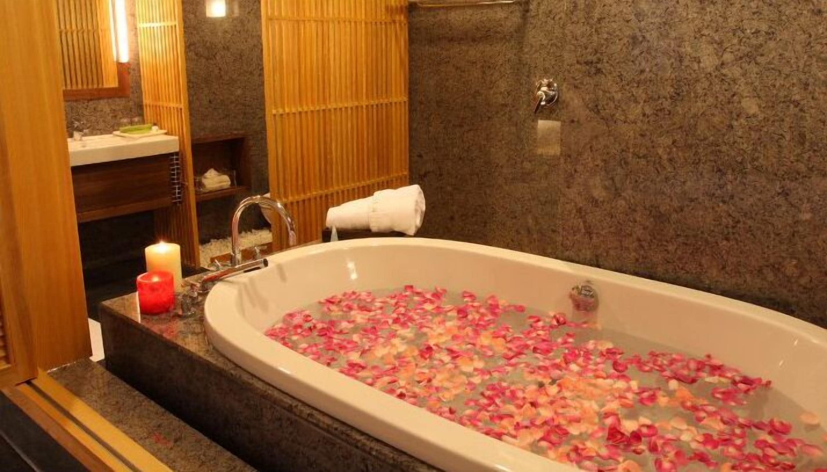 A bathroom with a bathtub filled with rose petals, a candle, and a towel hanging on the wall.