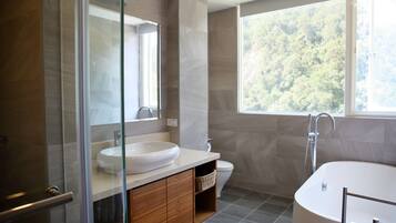 Un baño moderno con cabina de ducha de vidrio, una bañera independiente y un amplio ventanal con vistas al exterior.