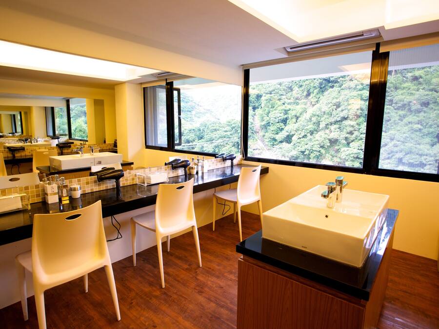 Una cocina moderna con una isla grande, sillas blancas y vistas a un bosque a través de amplios ventanales.