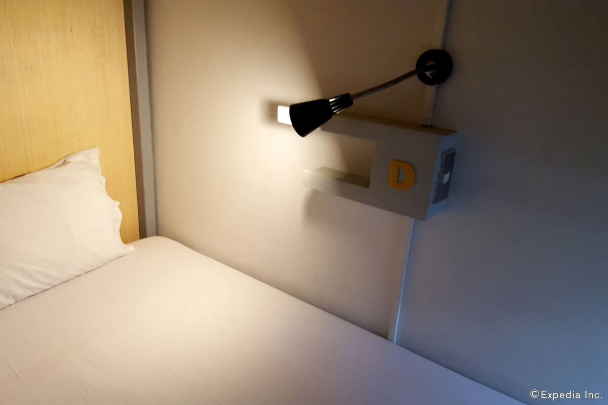 Yhden hengen sänky, jossa on valkoinen tyyny ja seinälle kiinnitetty yövalo.