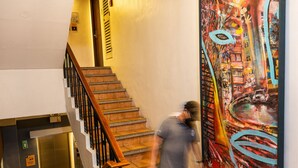 Un escalier avec une rampe en bois, un tableau accroché au mur et un extincteur posé sur le sol.