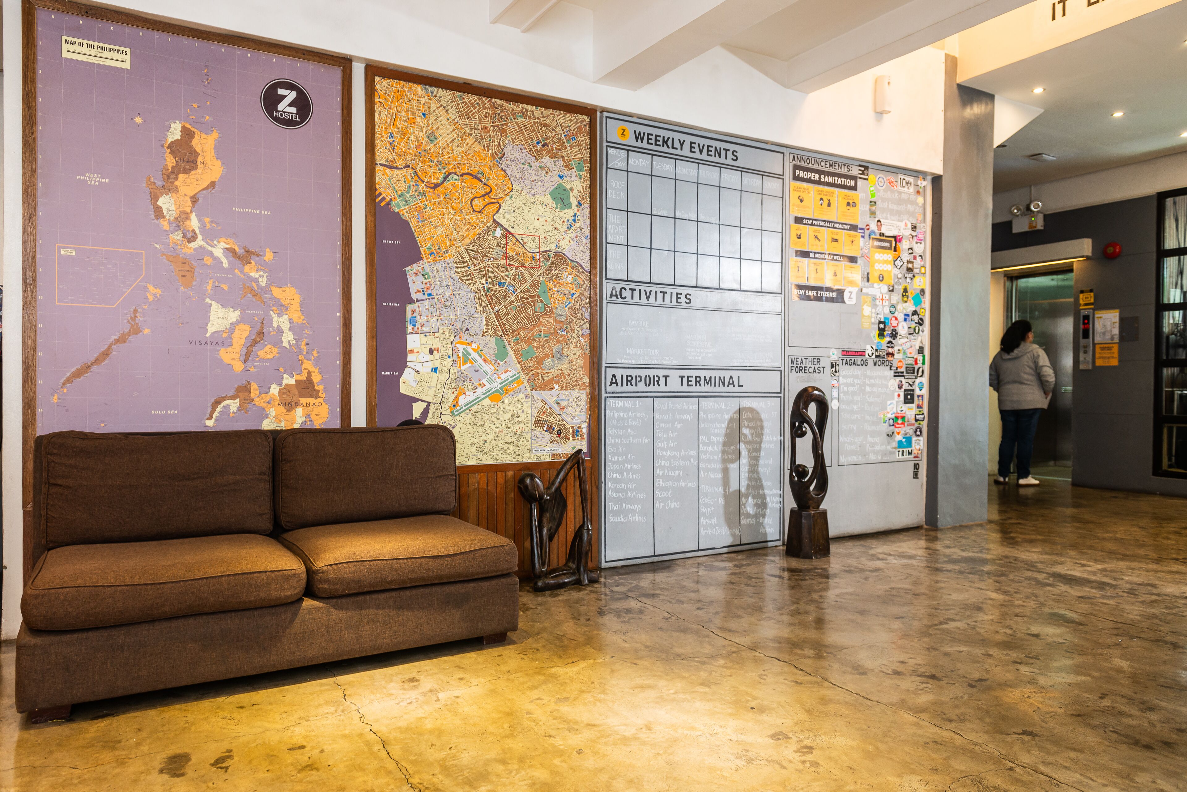 A lobby with a brown sofa, a map of the Philippines, a detailed city map, and a wall with a weekly events board.