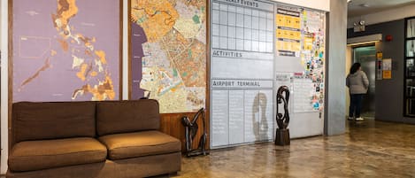 A lobby with a brown sofa, a map of the Philippines, a detailed city map, and a wall with a weekly events board.