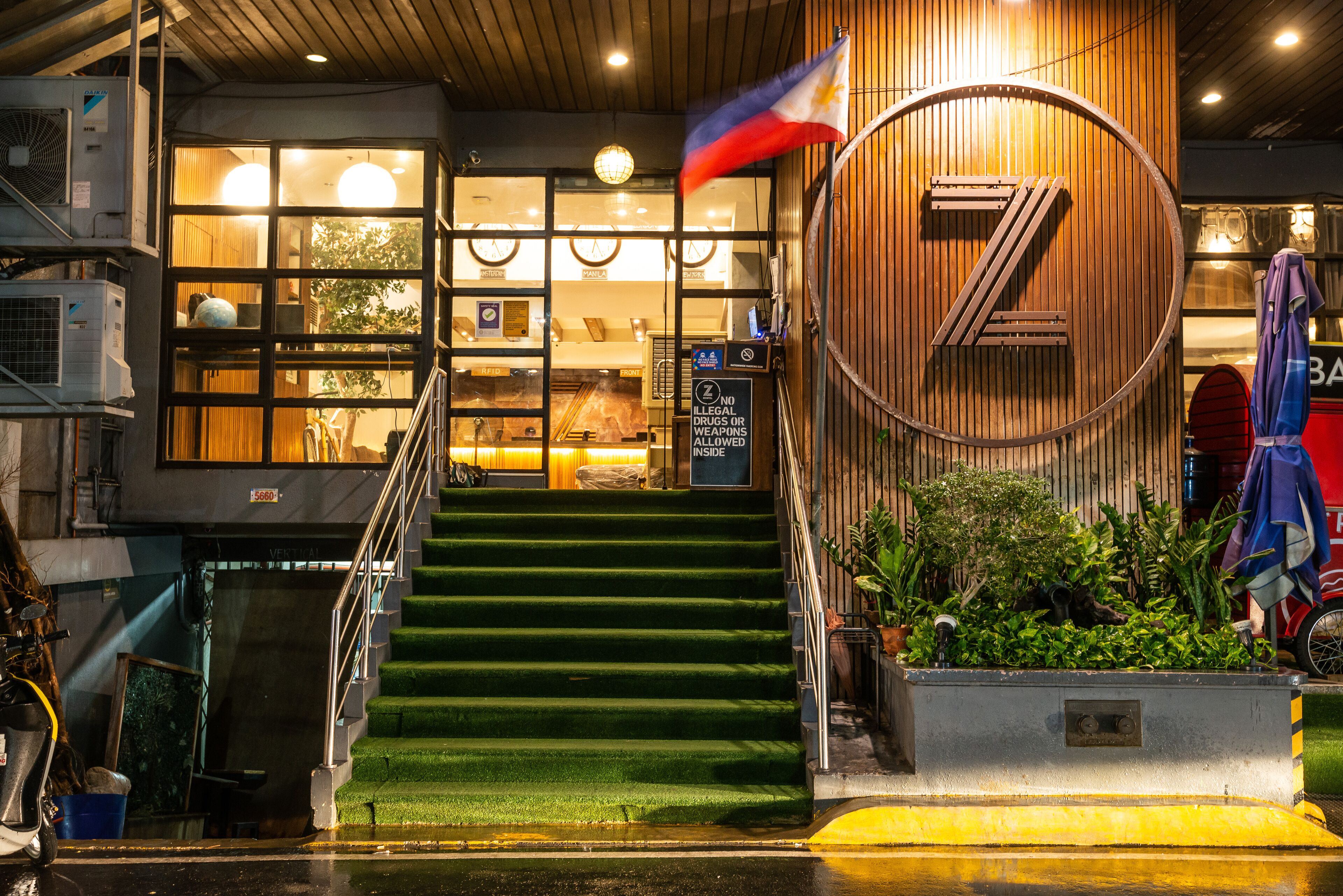 Entrada de hotel con fachada de madera, un gran logotipo circular y una escalera que conduce a la entrada.