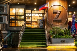 A hotel entrance with a wooden facade, a large circular logo, and a staircase leading to the entrance. - Z Hostel (Makati)