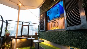 Un bar situé sur le toit, offrant une vue sur les gratte-ciel de la ville, un petit espace avec des tables et des chaises, et un vélo fixé au mur.