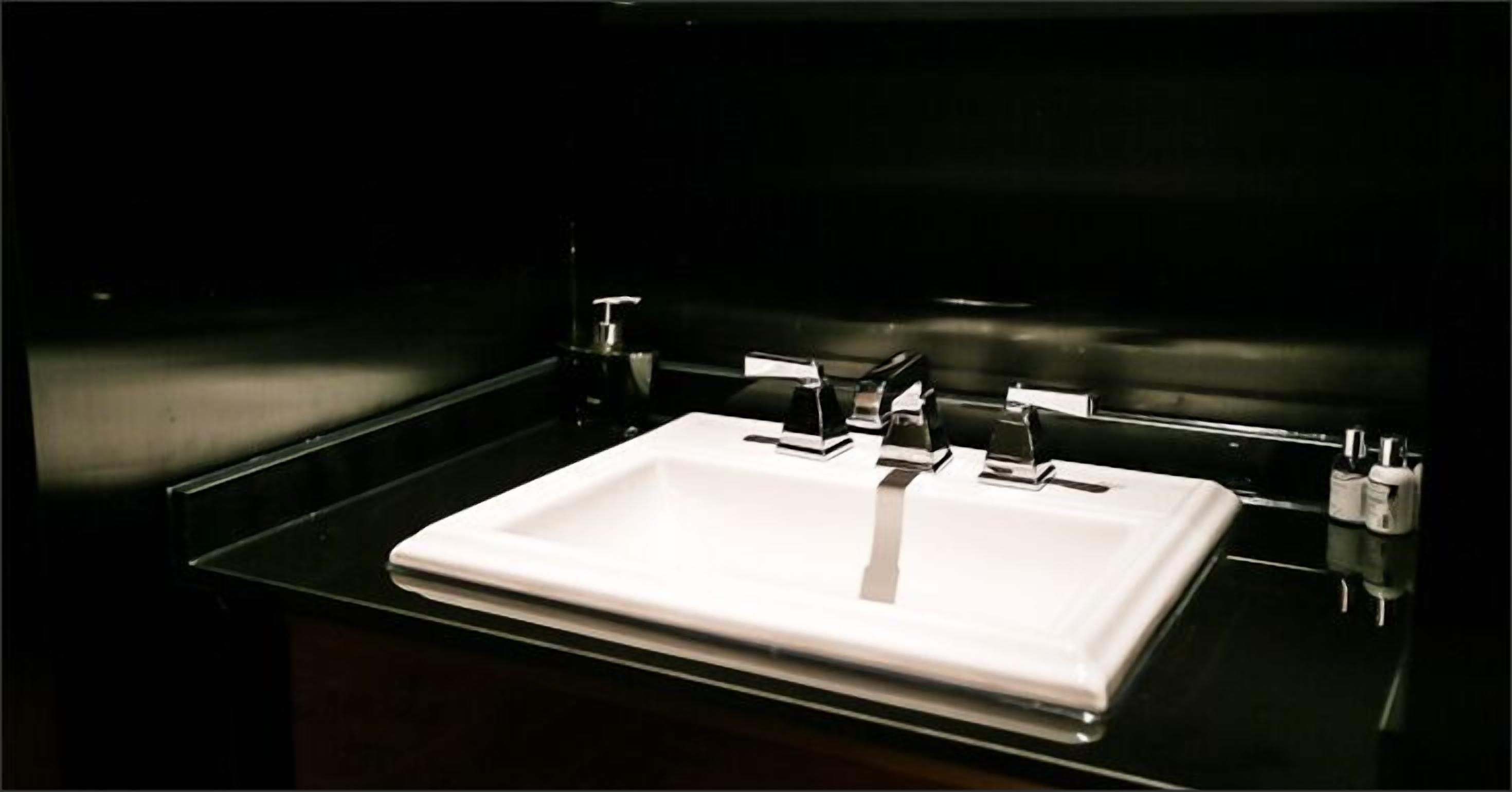 A modern bathroom with a white sink, chrome fixtures, and a dark background.