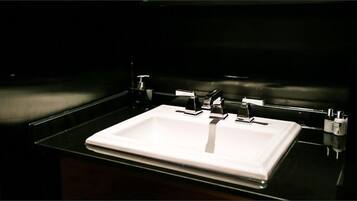 A modern bathroom with a white sink, chrome fixtures, and a dark background.