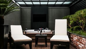 A modern outdoor seating area with two white cushioned chairs, a small table, and a built-in fireplace. - Amare Hotel Jakjeon (Incheon)