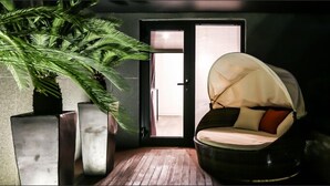 A room with a wooden floor, a large potted plant, a black chair with a canopy, and a door leading to an outdoor area. - Amare Hotel Jakjeon (Incheon)