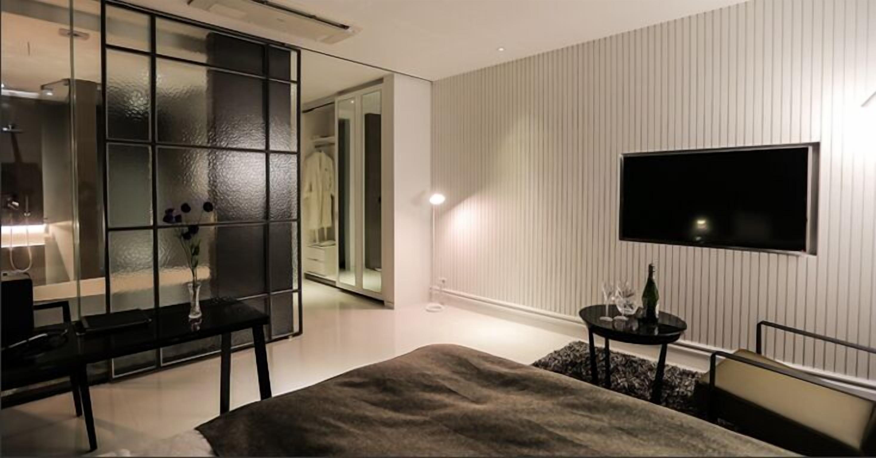 A modern bedroom with a large bed, a TV mounted on the wall, a bedside table, and a mirror.