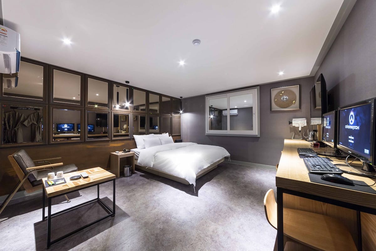 A modern hotel room with a large bed, a desk with a computer, a chair, and a window with a view.