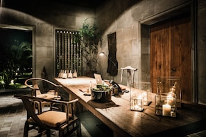 A dining area with a long wooden table, chairs, candles, and a laptop.