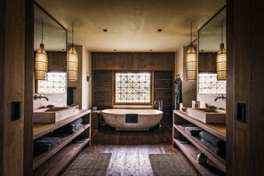 A spacious bathroom with a freestanding bathtub, wooden shelves, and a large window with a geometric pattern.