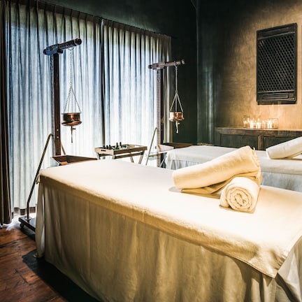 A spa room with two beds, a scale, candles, and a window with curtains.
