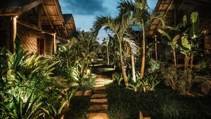 A pathway leading to thatched-roof structures surrounded by lush tropical vegetation. - Zannier Phum Baitang (Siem Reap)