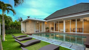 A modern house with a swimming pool, lounge chairs, and a well-maintained garden. - Villa Umah Putih (Canggu)