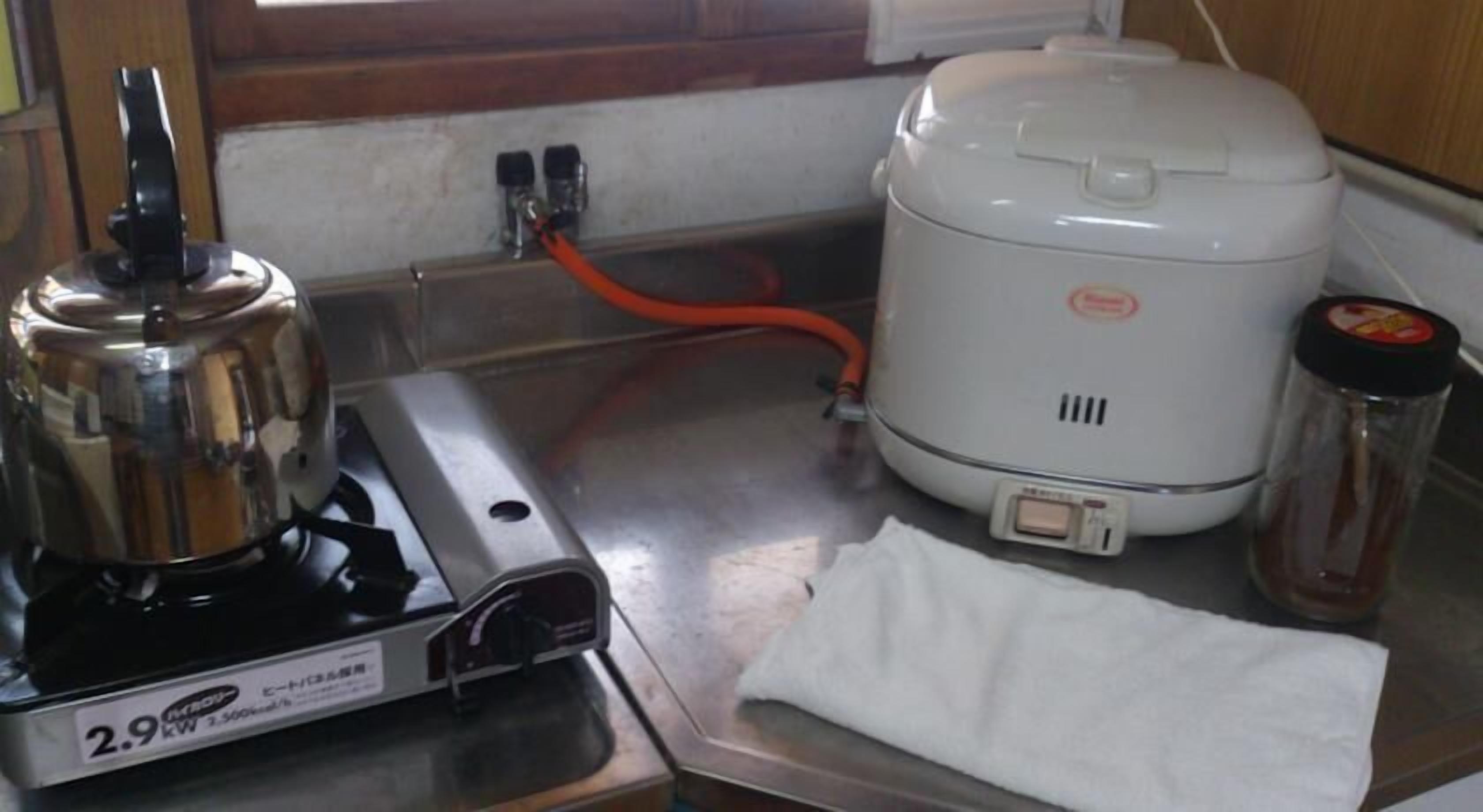 A kitchen with a kettle, a rice cooker, and a bottle of sauce on the counter.