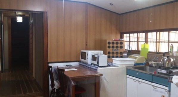 A compact kitchen with wooden walls, a microwave, a sink, and a small dining area with a chair.