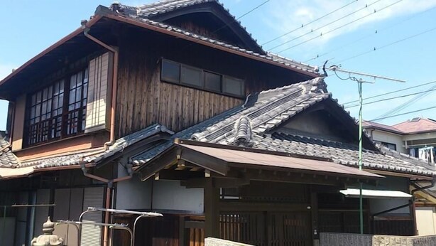 Ein traditionelles japanisches Haus mit geneigtem Dach, Holzfassade und einem sichtbaren Schornstein.