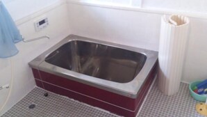Ein Badezimmer mit einer Edelstahlbadewanne, einem blauen Handtuch und einer weißen Toilette.