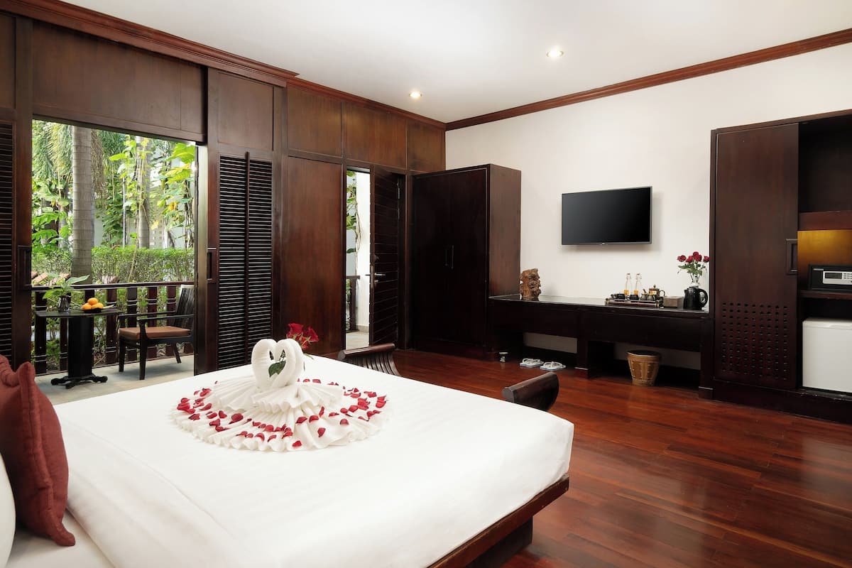 Quarto de hotel com cama, escrivaninha, televisão e vista para o verde lá fora.