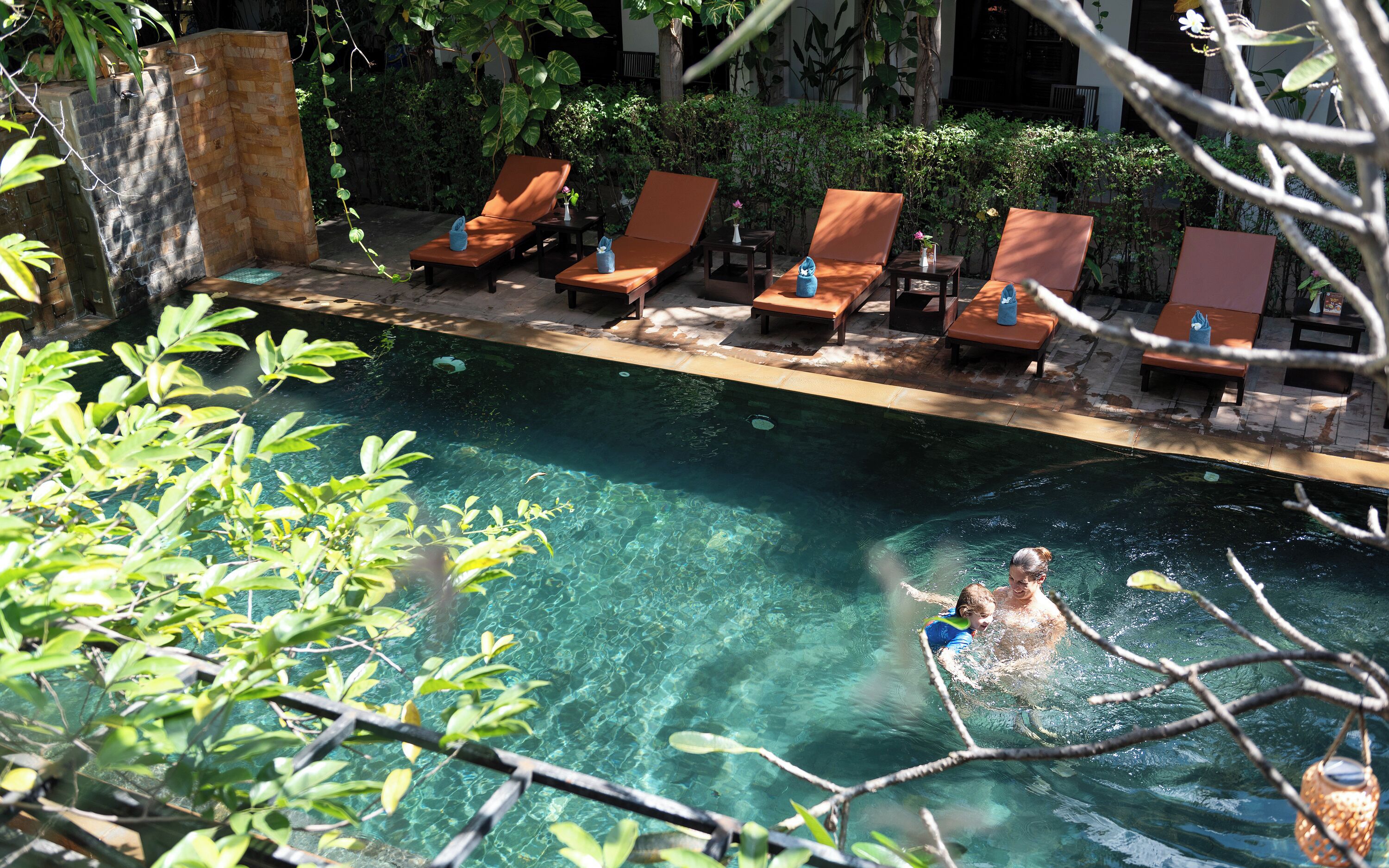 A clear pool with lounge chairs and a stone wall.