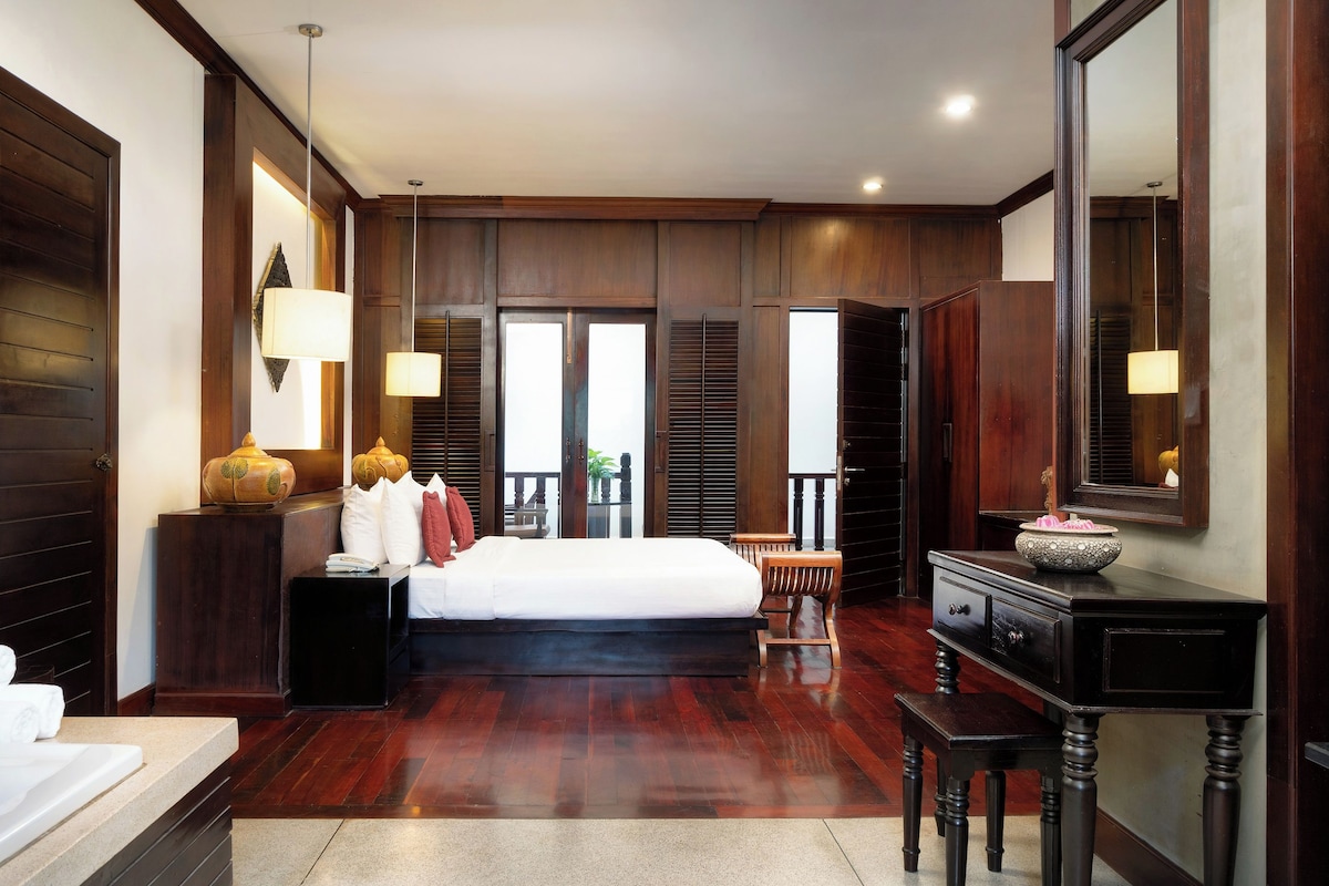 A spacious bedroom with a large bed, a vanity with a mirror, and a view of the balcony.