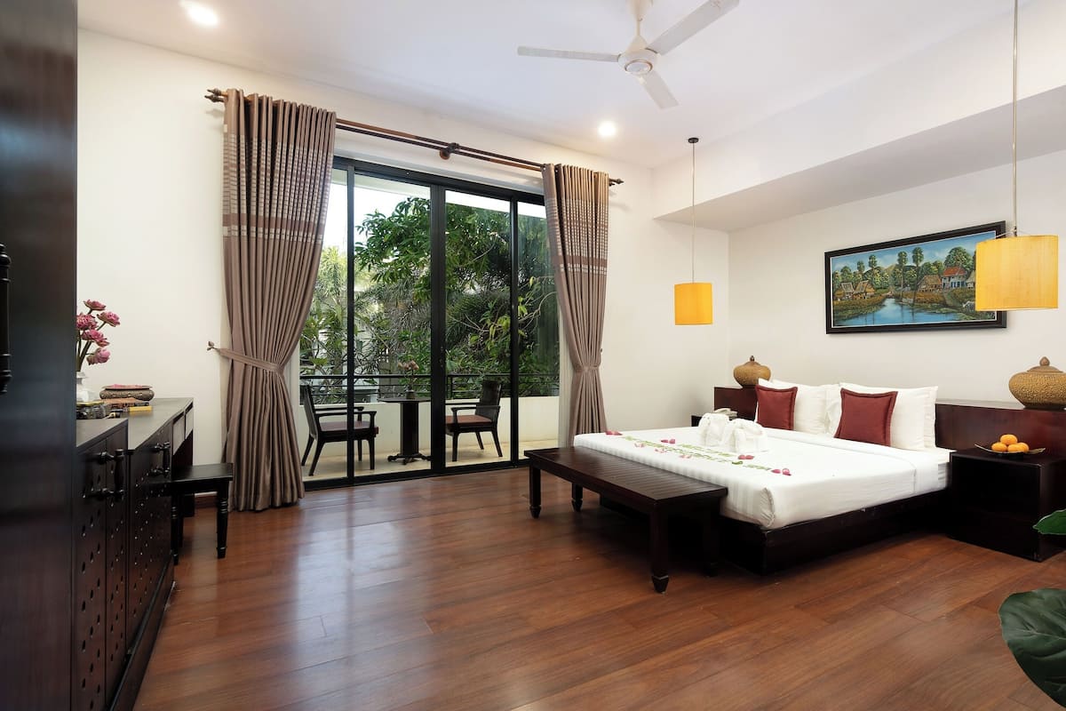 Quarto de hotel com cama, escrivaninha, cadeira, mesa e vista para o verde lá fora.