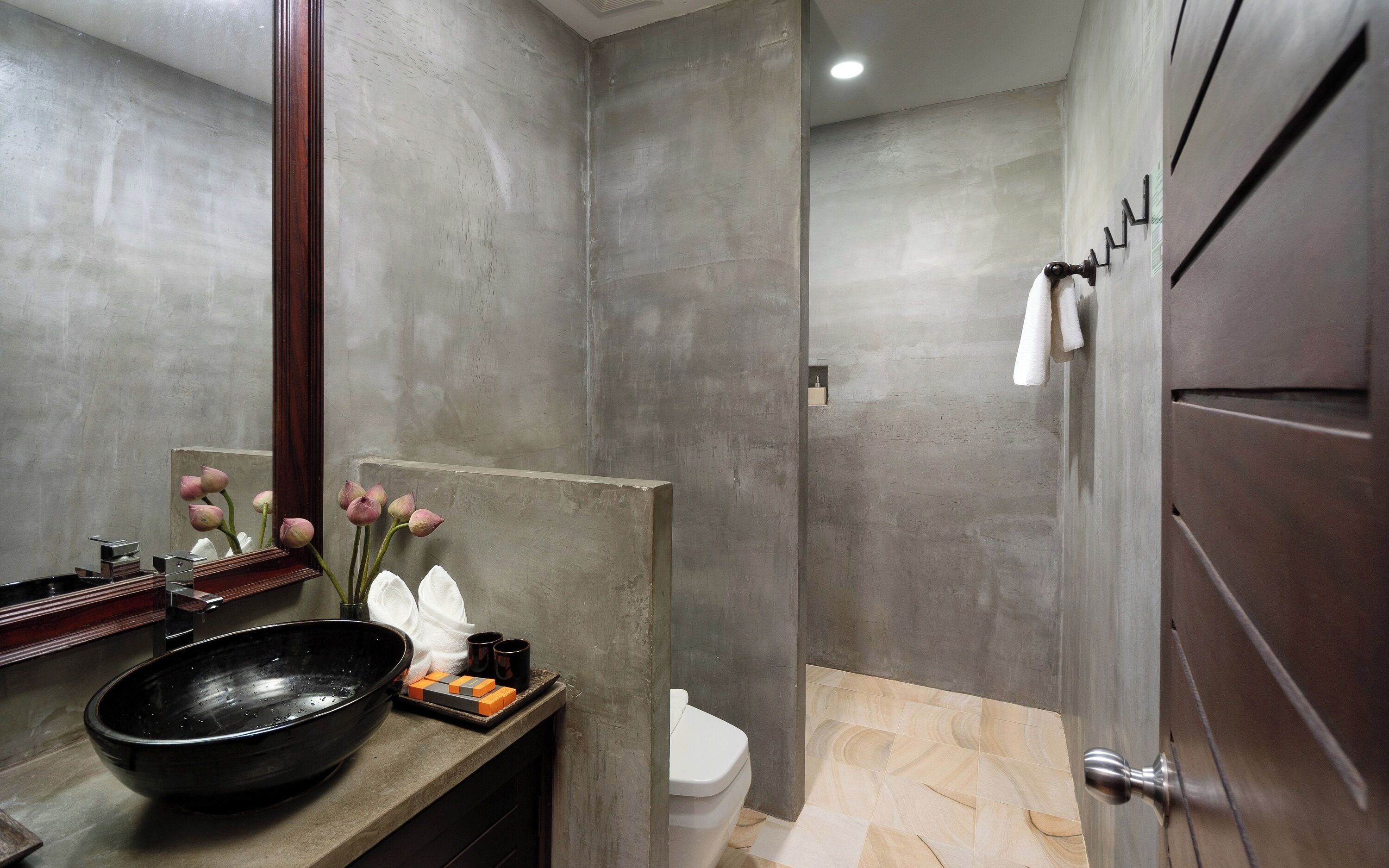 Une salle de bain moderne avec un grand miroir, un lavabo noir, des toilettes et un espace douche.