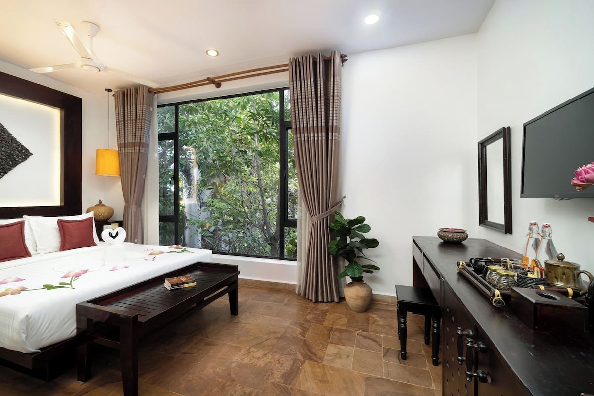 Quarto de hotel com cama, escrivaninha, televisão e janela com cortinas.