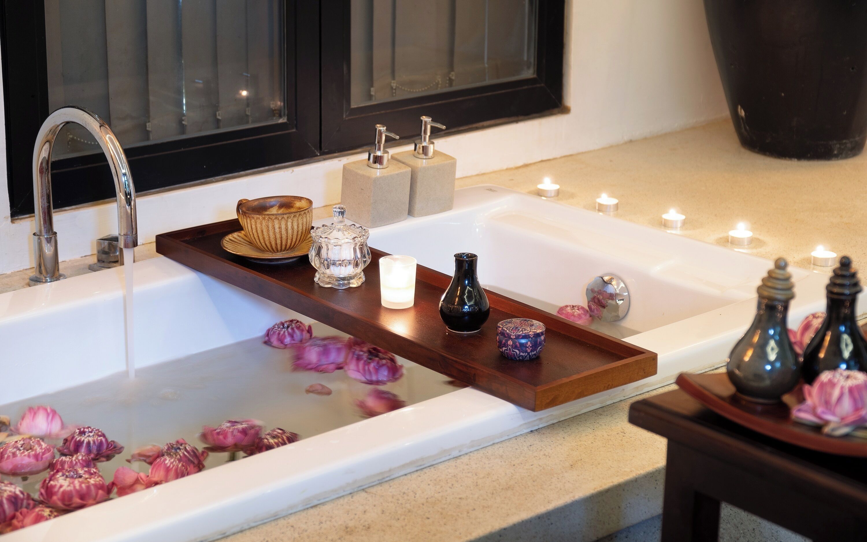 A bathroom with a bathtub, a wooden tray with various items, and candles.