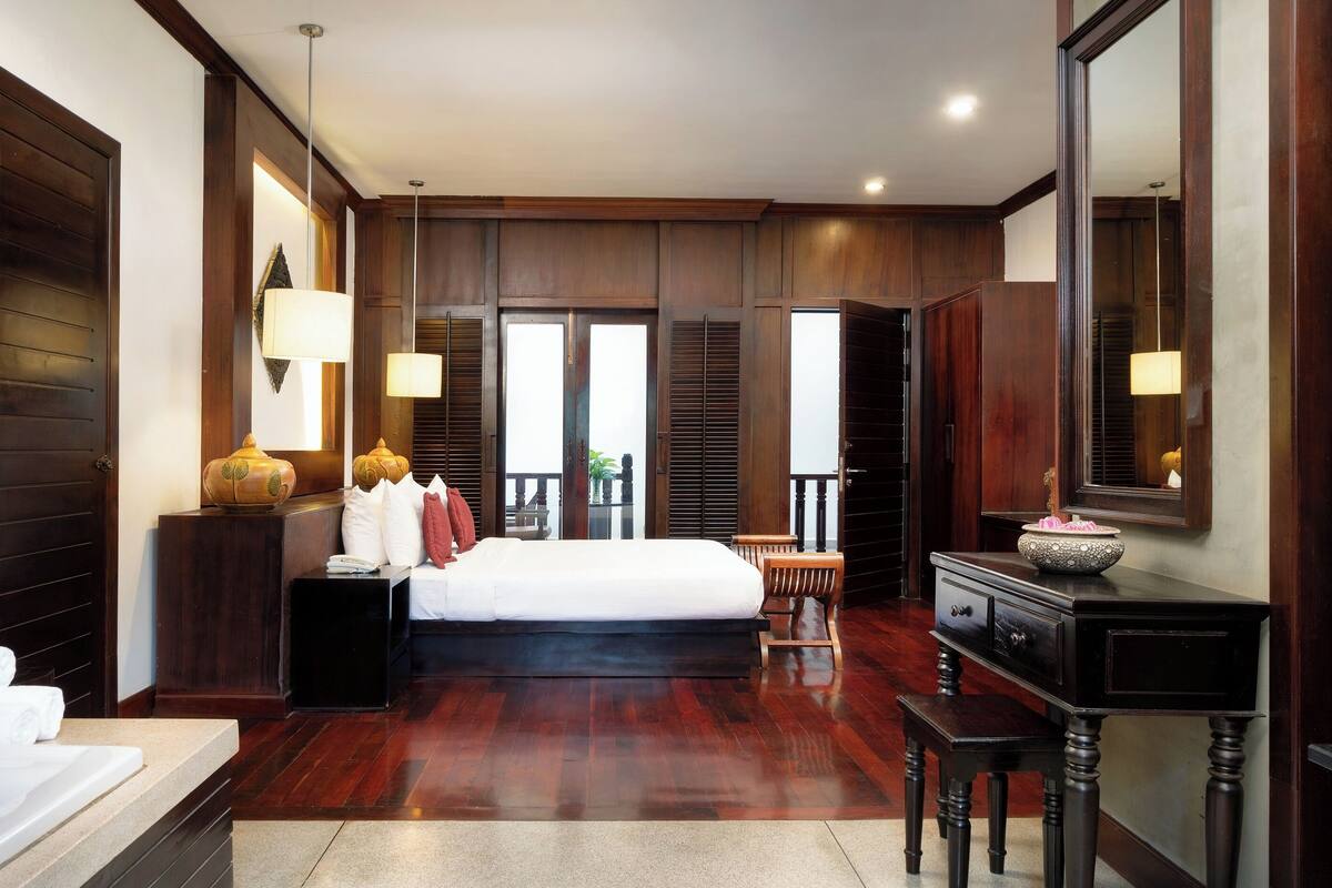 Quarto espaçoso com cama grande, piso de madeira, escrivaninha e espelho.