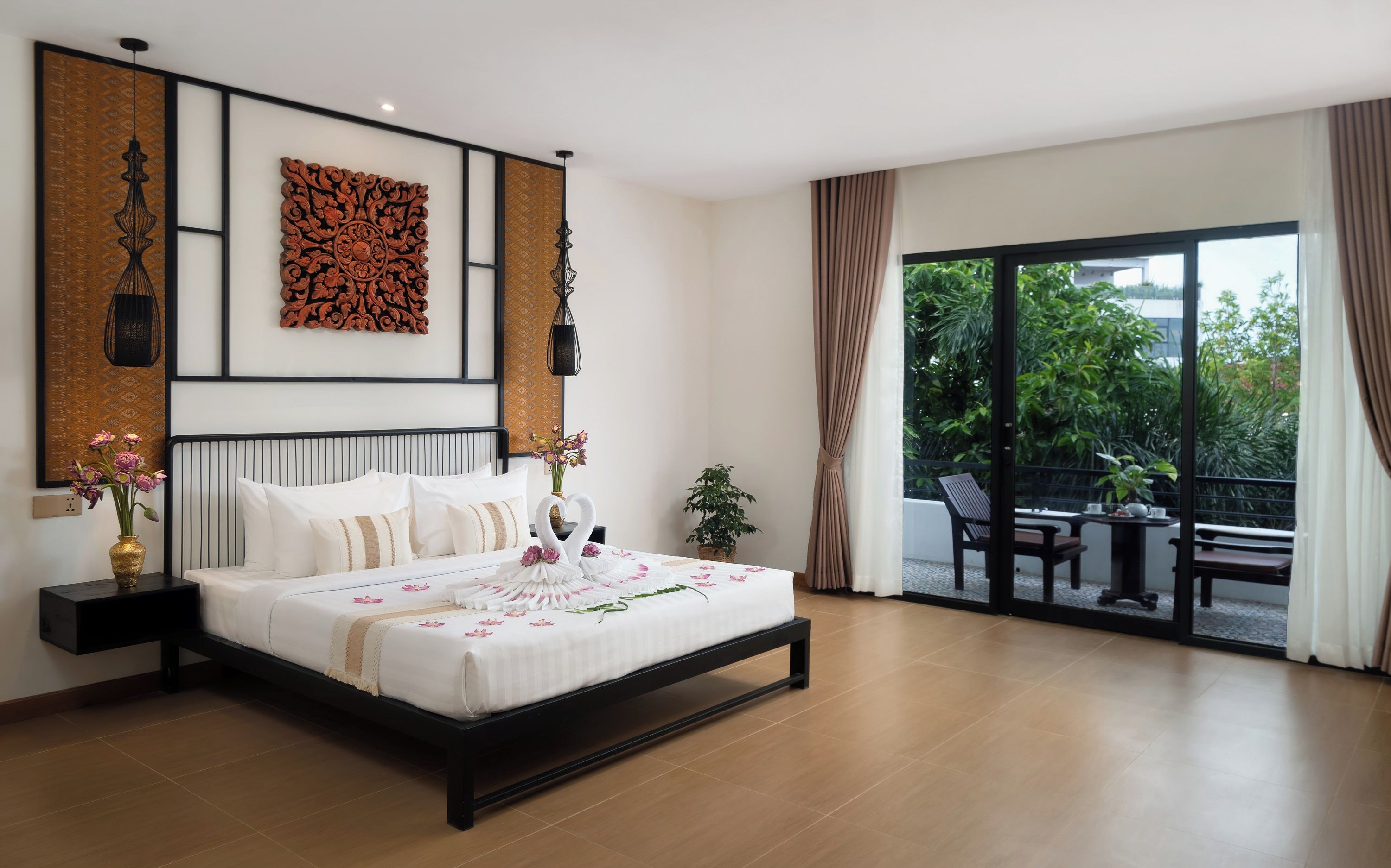 A modern bedroom with a large bed, a balcony with a table and chairs, and decorative wall art.