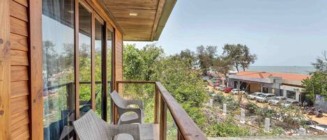 A balcony with wicker chairs and a view of a parking area and buildings.