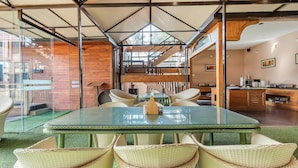A modern dining area with a glass table, wicker chairs, and a view of the kitchen and living space. - The Baga Beach Resort (Baga)