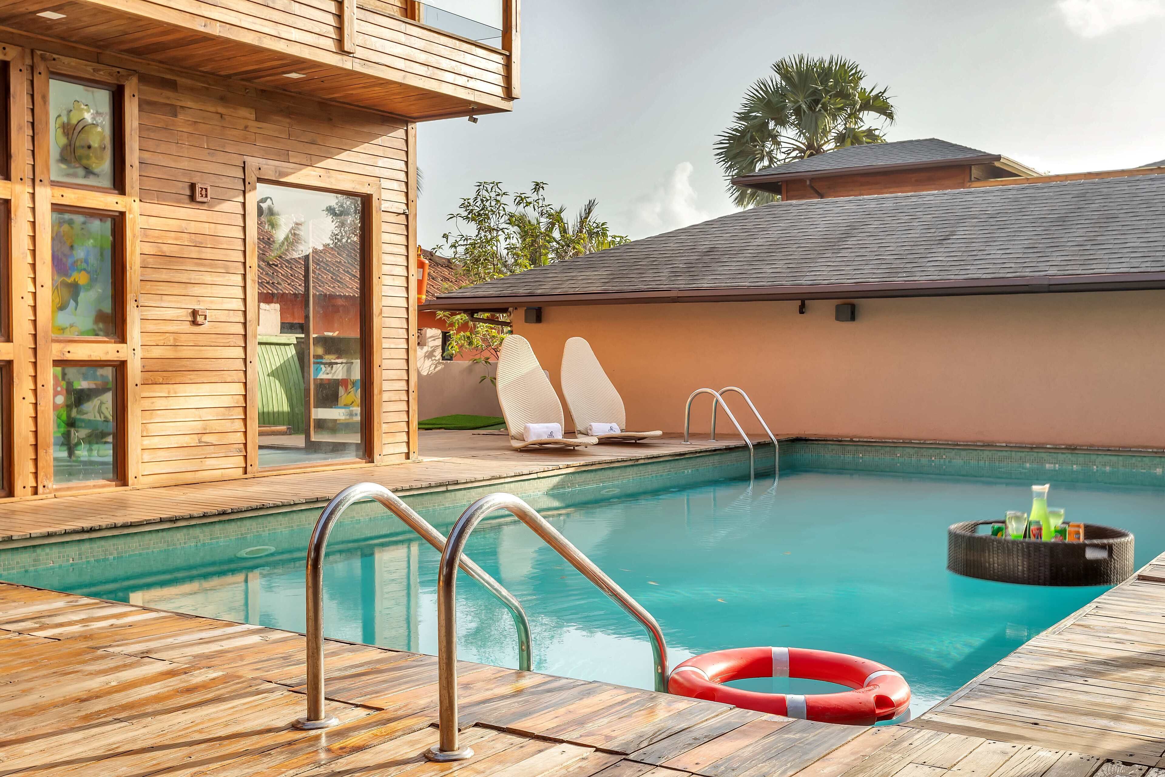 Un área de piscina con cubierta de madera, sillas de descanso y una chimenea flotante.
