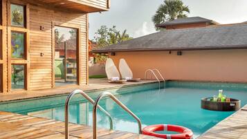 Un área de piscina con cubierta de madera, sillas de descanso y una chimenea flotante.
