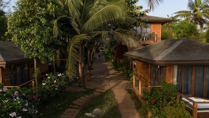 A pathway flanked by wooden buildings with a tropical garden and palm trees. - The Baga Beach Resort (Baga)