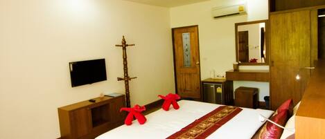 A hotel room with a large bed, wooden flooring, a ceiling fan, a mounted TV, a wooden wardrobe, and a mirror.