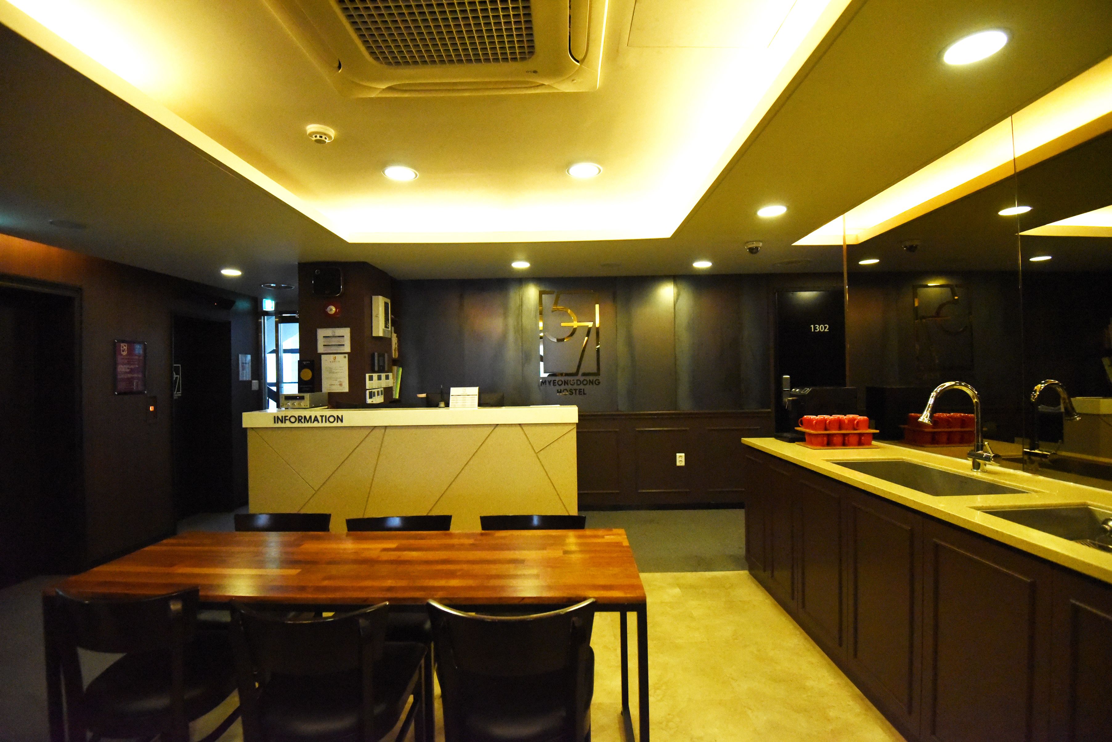 A modern kitchen with a wooden dining table and chairs, a built-in sink, and a counter with an information station.