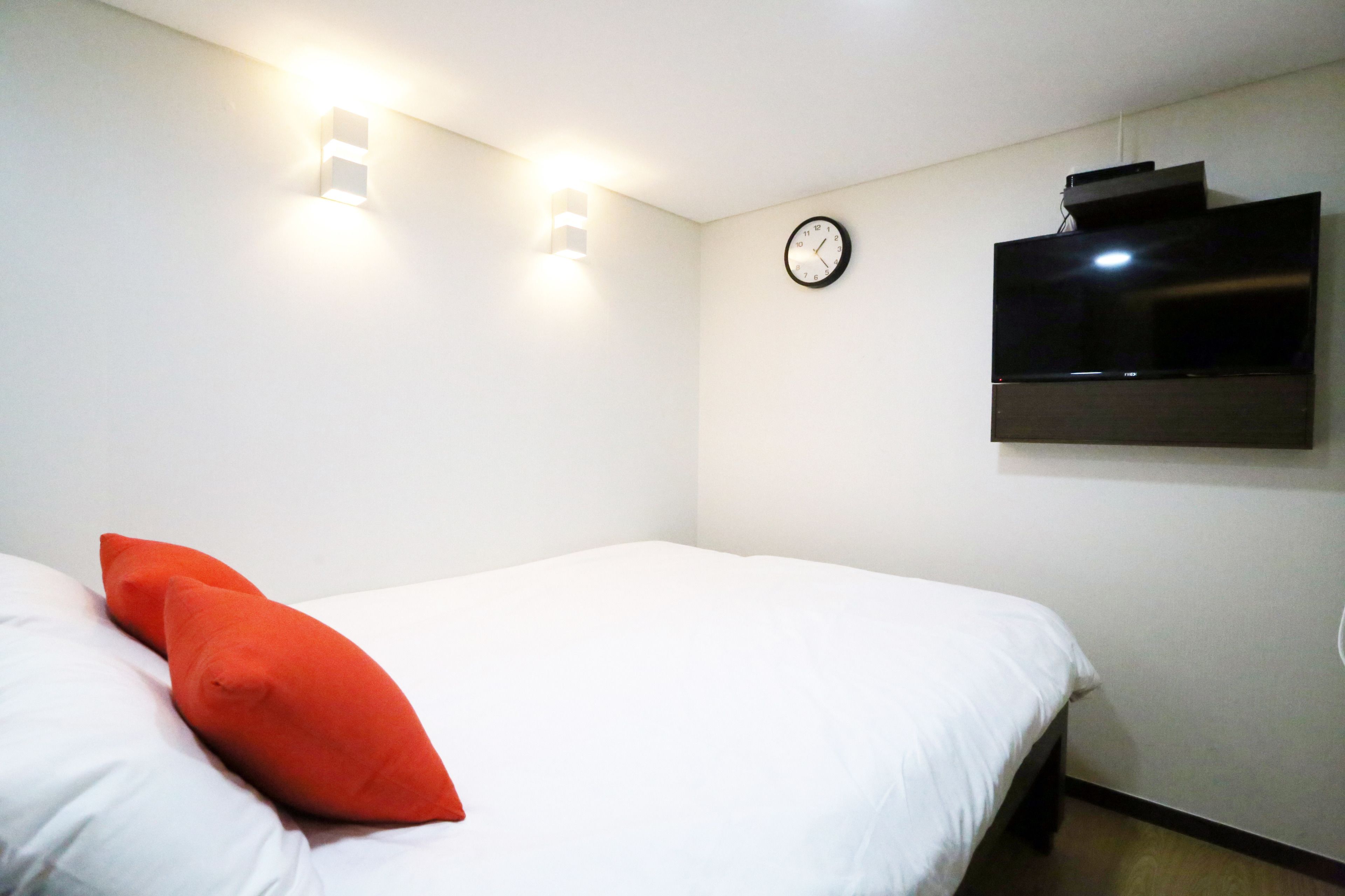 A hotel room with a bed, a wall-mounted TV, and a clock.
