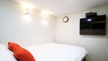 A hotel room with a bed, a wall-mounted TV, and a clock.