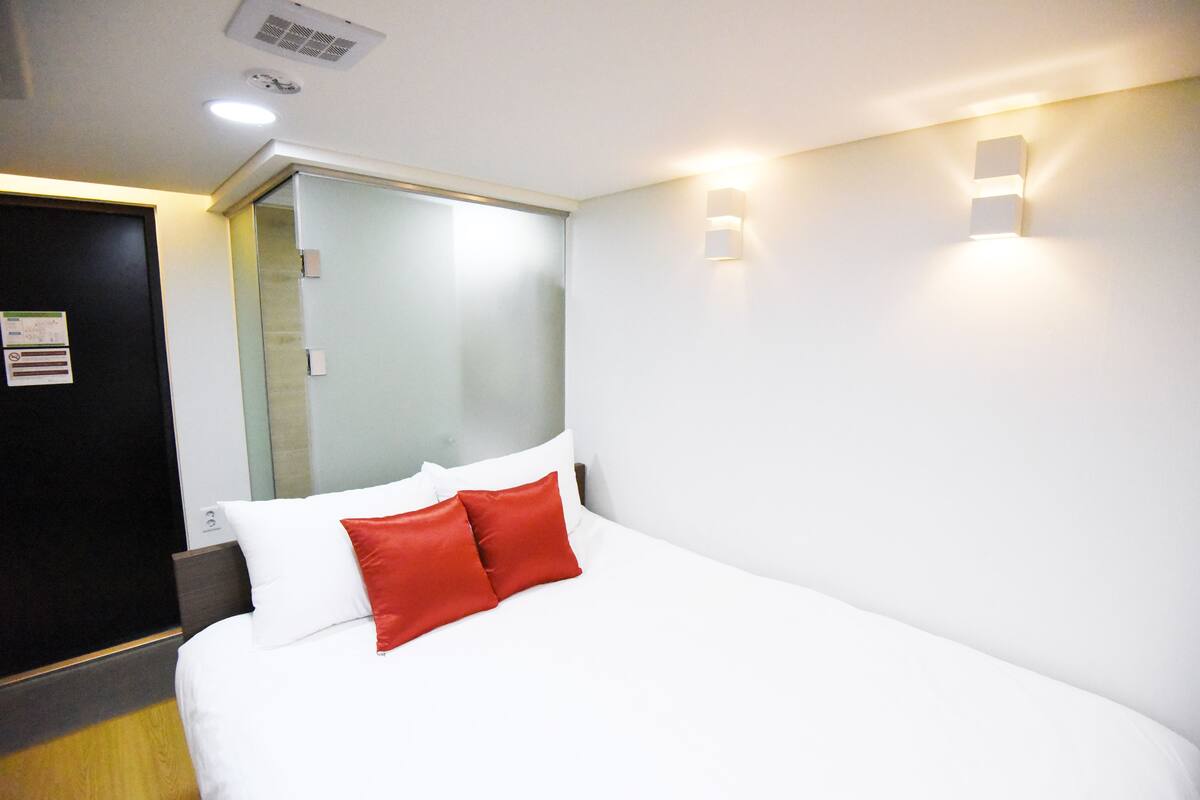 Habitación de hotel con cama, puerta y lámpara fijada a la pared.