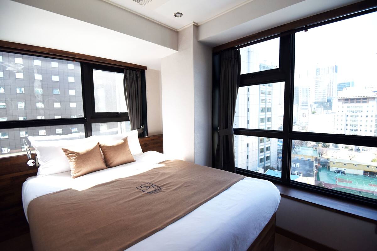 Una habitación de hotel con una cama grande, una mesita de noche y un ventanal con vistas a la ciudad.
