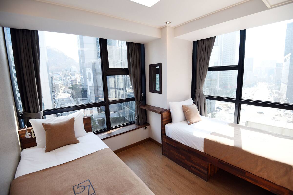 Habitación de hotel con dos camas, ventanas amplias y vista a la ciudad.
