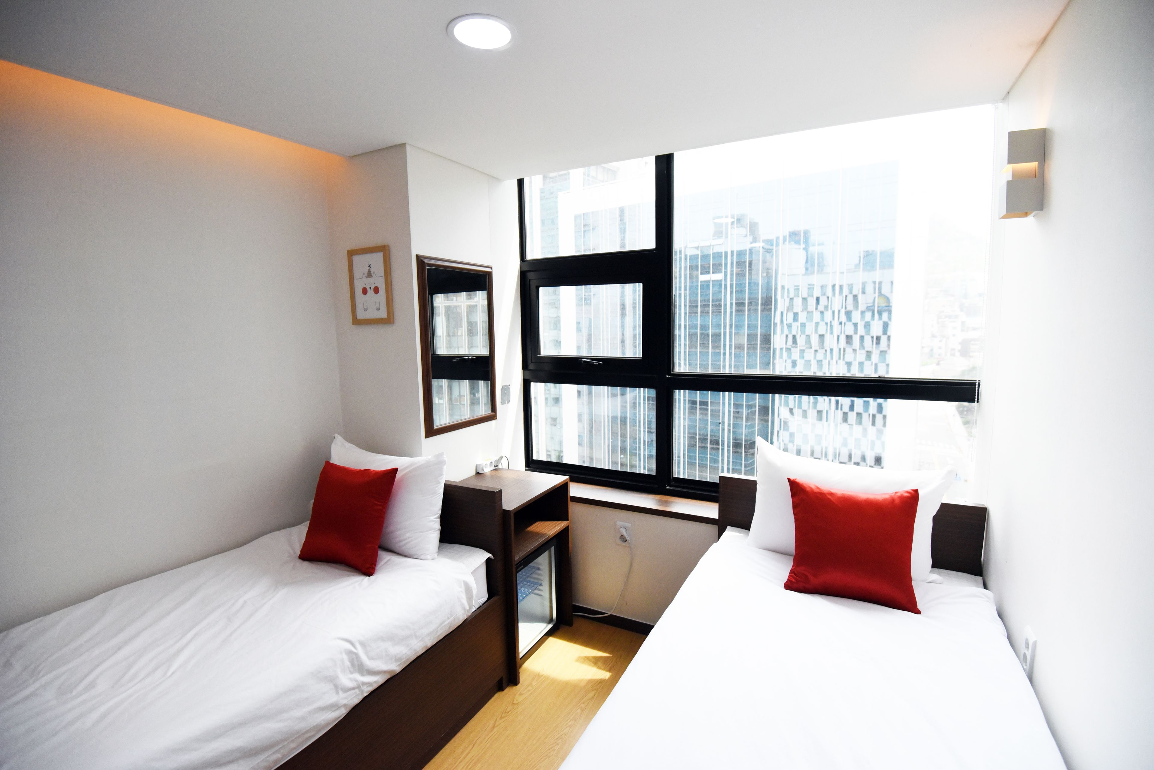 Une chambre d’hôtel moderne avec deux lits simples, un bureau et une grande fenêtre donnant sur la ville.