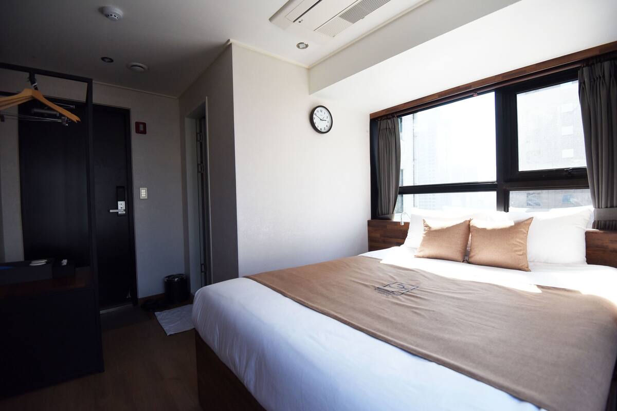 Una habitación de hotel con una cama, un reloj, una ventana y una puerta.
