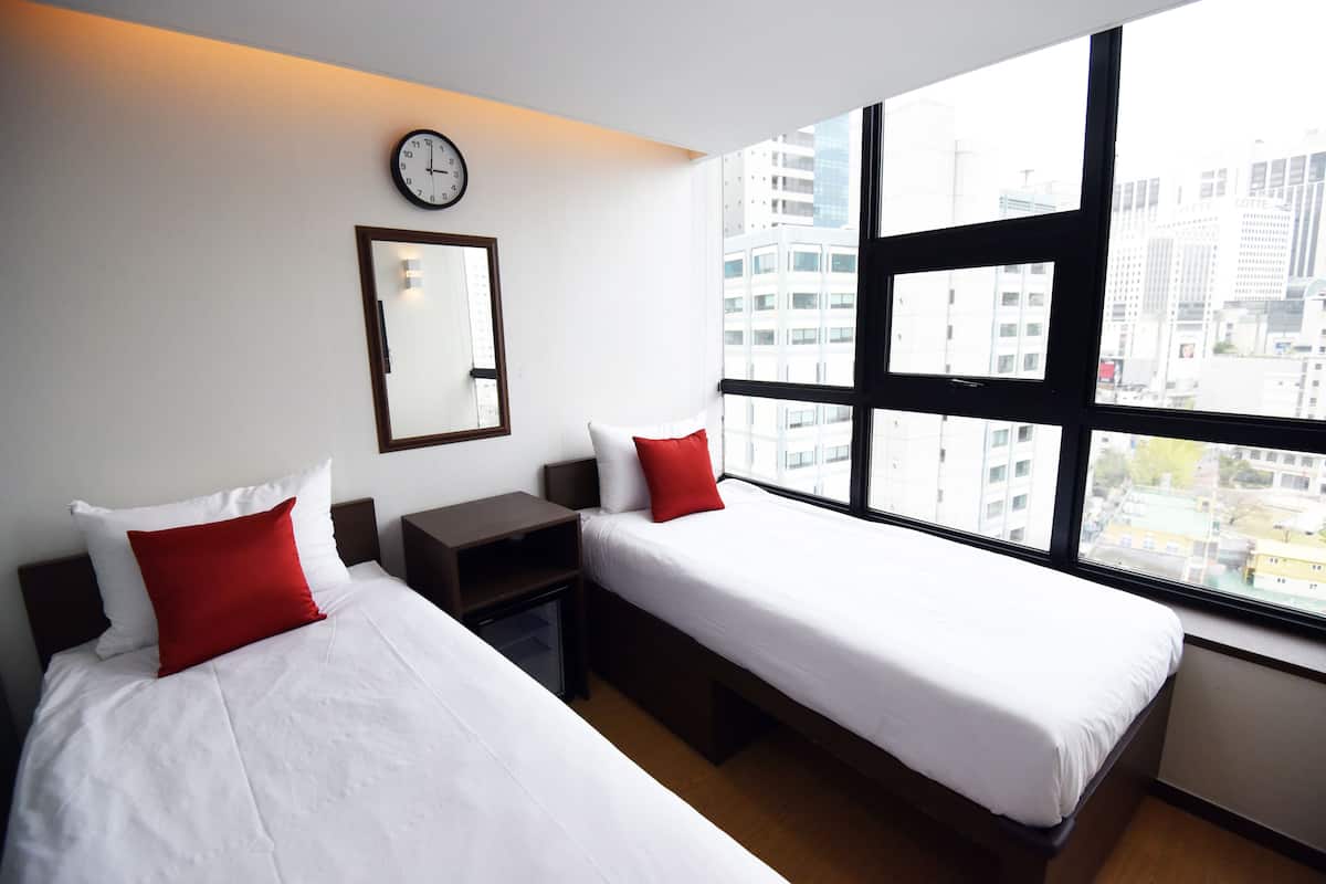 Habitación de hotel con dos camas, un ventanal grande, un reloj y un espejo en la pared.